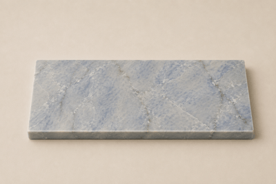 Azul Emerald Accessoireplank van natuursteen met blauwgrijze tinten en verfijnde witte aders op een rustige beige achtergrond.