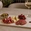 Glencoe Signature Tapasplank met luxe borrelhapjes op een sfeervol gedekte eettafel naast een glas witte wijn.