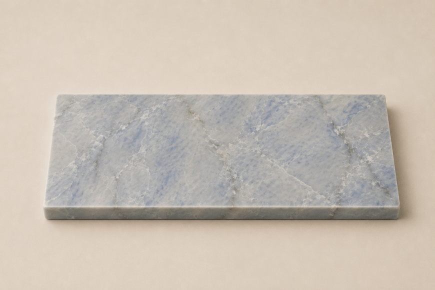 Azul Emerald Accessoireplank van natuursteen met blauwgrijze tinten en verfijnde witte aders op een rustige beige achtergrond.