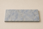 Azul Emerald Accessoireplank van natuursteen met blauwgrijze tinten en verfijnde witte aders op een rustige beige achtergrond.