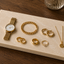 Rechthoekige Glencoe natuurstenen plank met gouden sieraden, horloge, ringen en ketting.